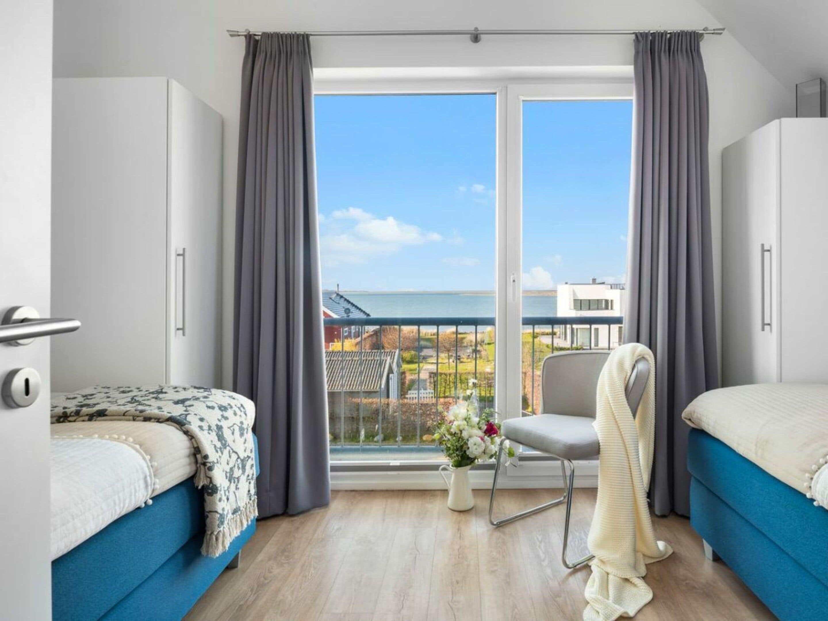 Ein modernes Hotelzimmer mit zwei Betten, einem Balkon mit Meerblick und einem Sessel.