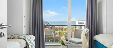 A modern hotel room with two beds, a balcony with a view of the sea, and a chair.