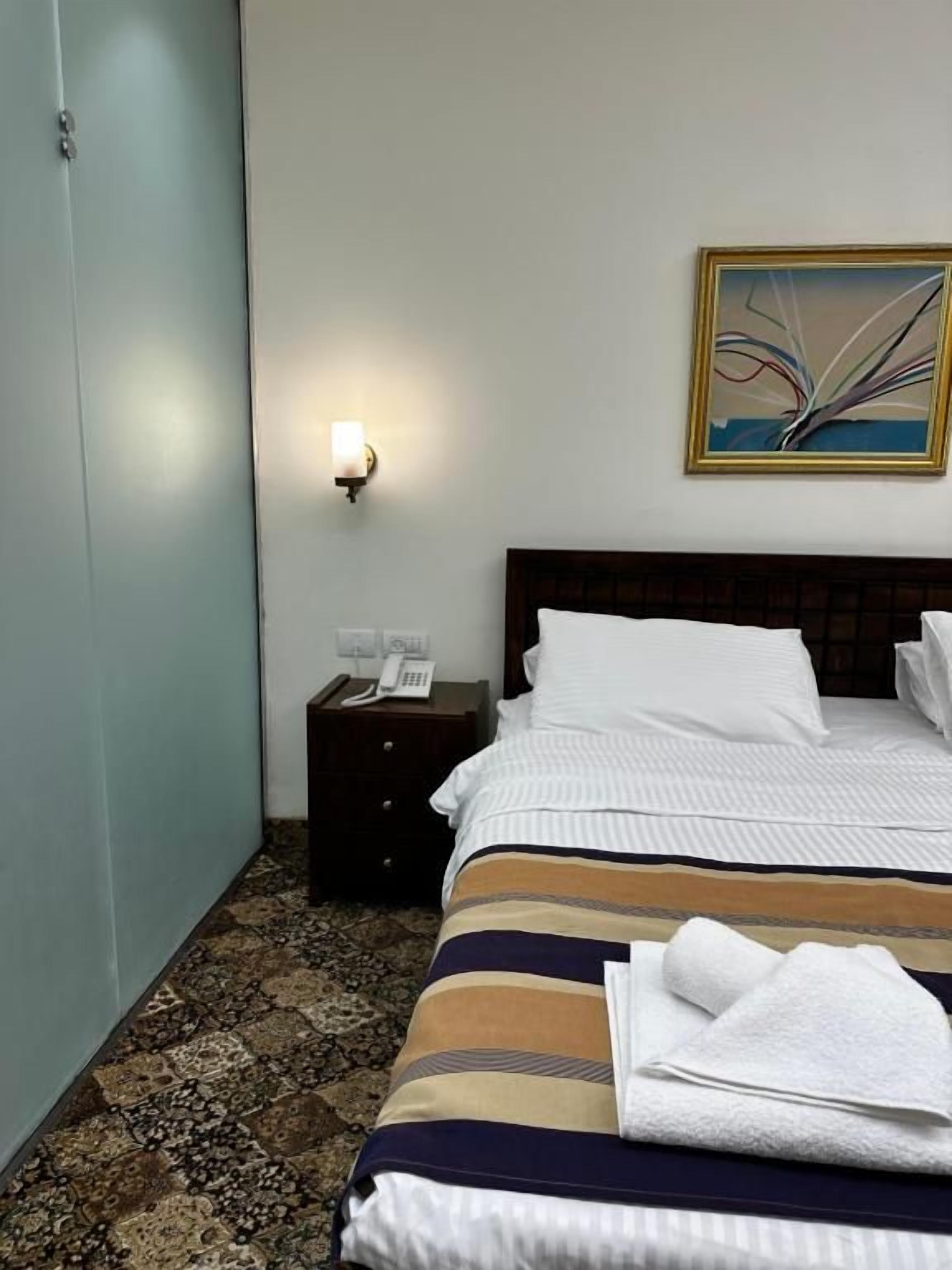 A hotel room with a bed, a nightstand, a telephone, and a painting on the wall.