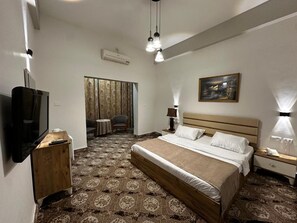 A hotel room with a large bed, a television, a desk, and a chair. - Shepherd Hotel (Bethlehem)