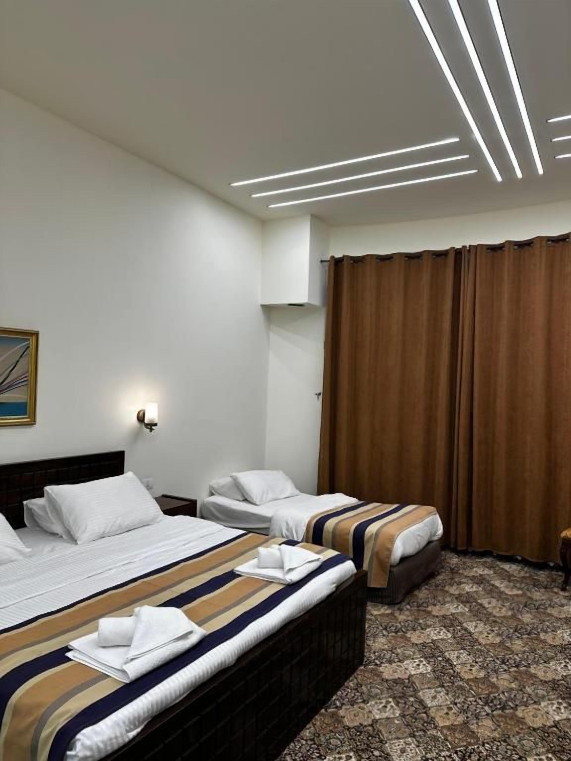 Habitación de hotel con dos camas, cabecero, luz de pared, cortina y alfombra estampada.
