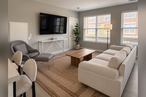 A modern living room with a sofa, armchair, coffee table, and a flat-screen TV mounted on the wall. - SUBLET — LUXURY FURNISHED RENTAL IN ENGLEWOOD, NJ (Englewood)