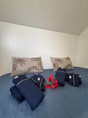 A bed with two pillows, a blue blanket, and a small bouquet of flowers. - To complete (Saint-Francois)