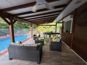A covered outdoor seating area with a pool, wicker furniture, and a wooden wall with a lion carving. - To complete (Saint-Francois)