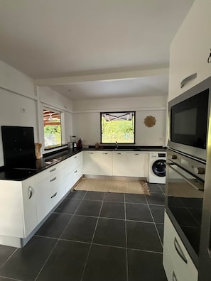 A modern kitchen with a black countertop, white cabinets, a built-in oven, and a large window. - To complete (Saint-Francois)