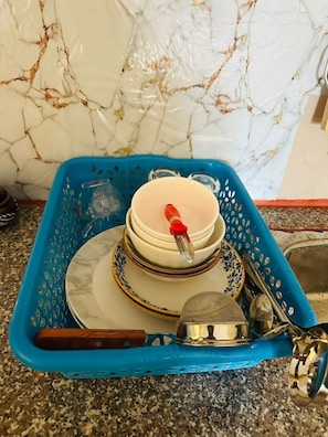 En køkkenbordplade med en blå plastkurv fyldt med stablede skåle, en ske og en si.