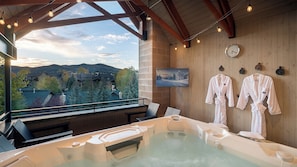 A spa area with a hot tub, wooden walls, a clock, and a view of a snowy landscape. - Hot Tub + Private Shuttle - Hawk's View Chalet (Steamboat Springs)