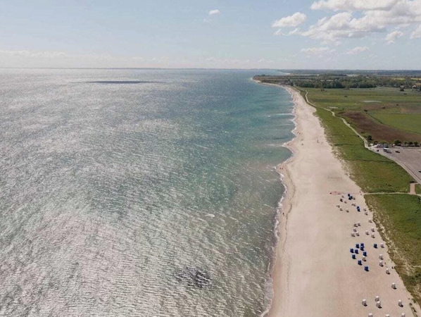 An aerial view of a beach with a clear shoreline, a parking area with several vehicles, and a distant view of the coastline. - Holiday Apartment With 2 Bedrooms (Kappeln)