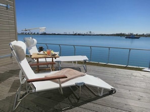 A deck with lounge chairs and a table, overlooking a calm body of water. - Holiday Apartment With 2 Bedrooms (Kappeln)