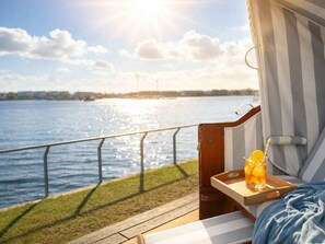Terraza con vista a un cuerpo de agua, un vaso de bebida con rodaja de limón y una cortina a rayas.