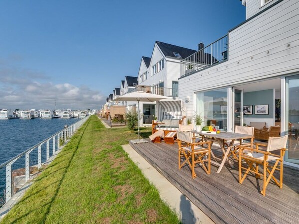 Ein Ufergrundstück mit Terrasse, Gartenmöbeln und Blick auf das Wasser.