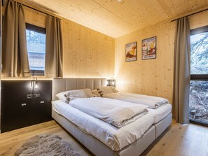 Ein Schlafzimmer mit Holzboden, einem Bett mit weißer Bettwäsche, einem Fenster mit Vorhängen und zwei gerahmten Bildern an der Wand.