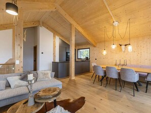 Ein modernes Interieur mit Holzbalkendecke, einem Essbereich mit grauen Stühlen, einer Couch mit Kissen und einem rustikalen Holztisch.