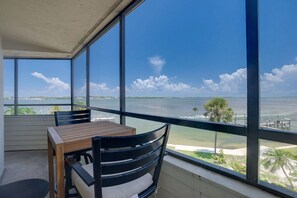 A balcony with a table and chairs, overlooking a body of water and a distant shoreline. - Bay Views & Heated Pool | Coastal 2BR Retreat (Bradenton Beach)