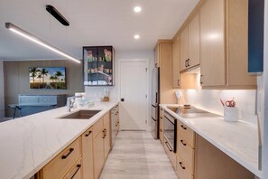 A modern kitchen with a long countertop, wooden cabinets, and a built-in oven. - Bay Views & Heated Pool | Coastal 2BR Retreat (Bradenton Beach)