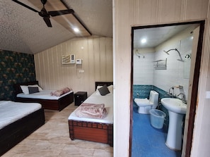 Quarto com duas camas, um ventilador de teto, uma mesinha de cabeceira e banheiro com pia e vaso sanitário.