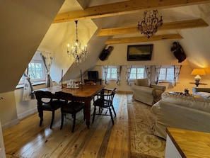 Ein gemütlicher Dachbodenwohnraum mit Esstisch, Stühlen, einer Couch und einem Kronleuchter.