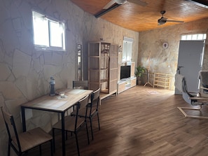 A room with a wooden dining table, chairs, a TV stand, and a stone wall.
