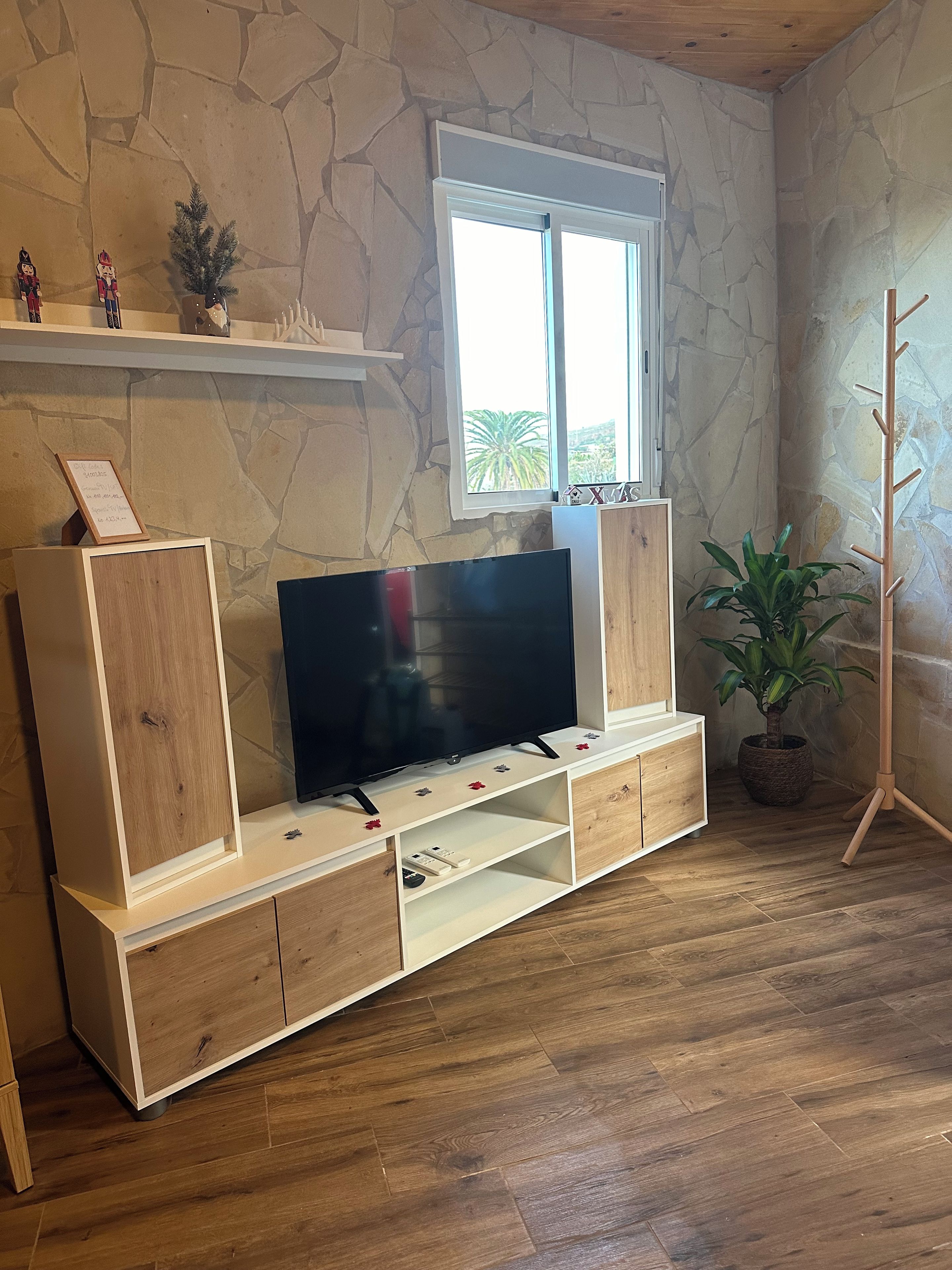 Un mueble de madera con un televisor de pantalla plana, una pared de piedra, una ventana y un perchero.