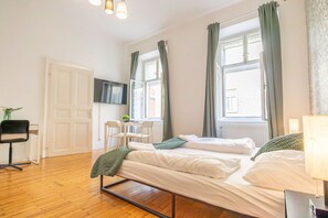 Ein Schlafzimmer mit einem Bett, einem Schreibtisch, einem Stuhl, einem Fernseher und zwei Fenstern mit Vorhängen.