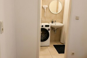Ein kleines Badezimmer mit Waschmaschine, Waschbecken und Spiegel.