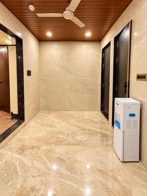 A hallway with marble flooring, a ceiling fan, and a water dispenser. - S.G.P - Premium Dormitory  (Mathura)