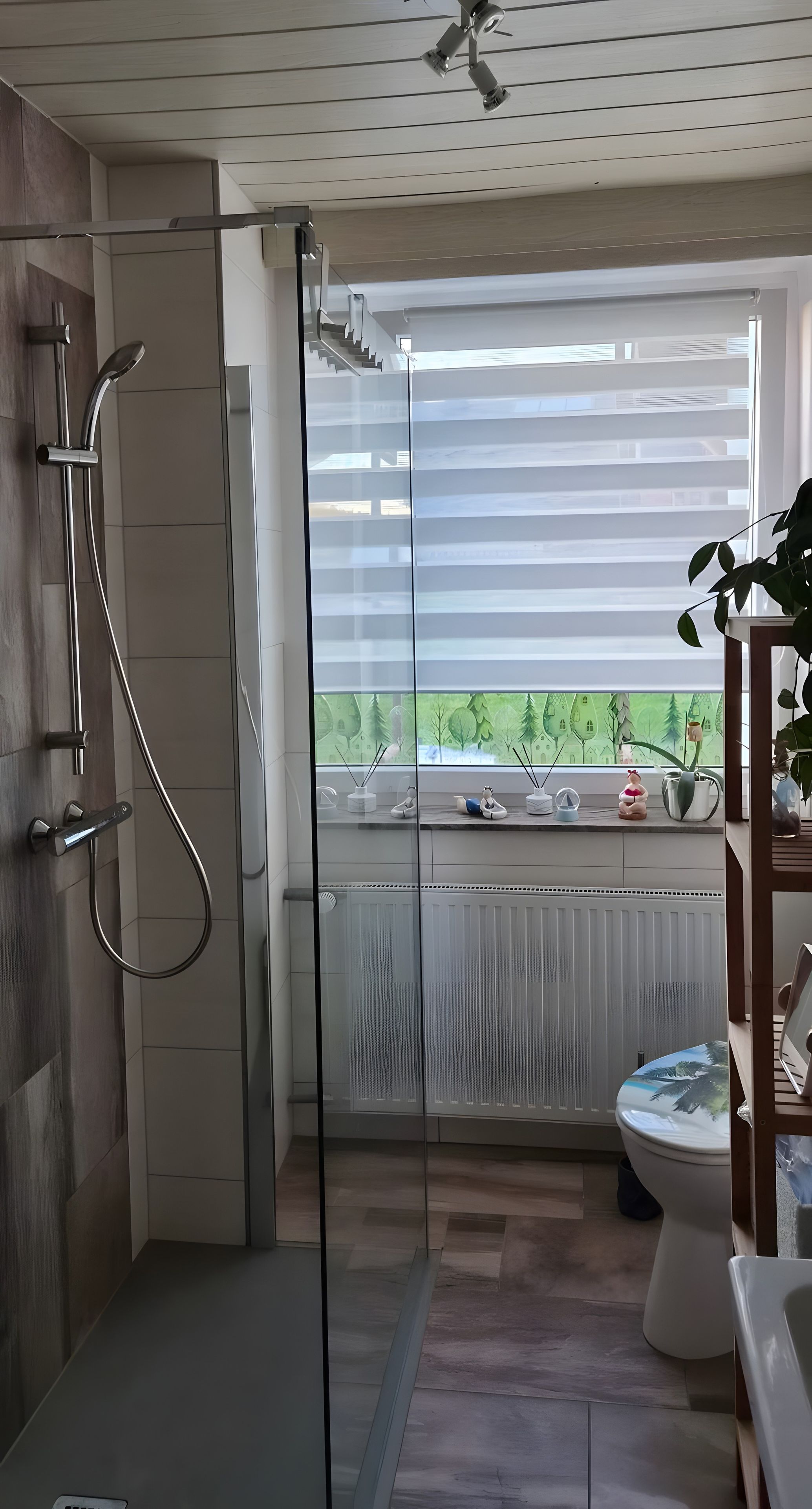 Un baño moderno con cabina de ducha de vidrio, inodoro y ventana con vista a zonas verdes.