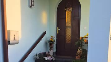 A staircase leading to a door with a 'HEROST' sign, a wall-mounted light, and potted plants.