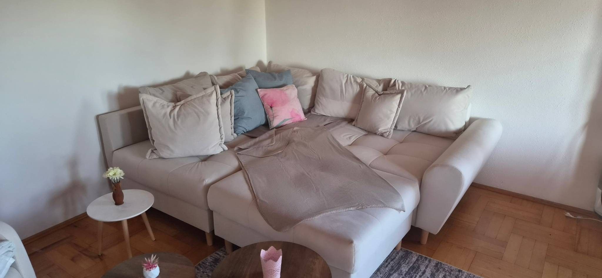 A living room with a beige sofa, a small round table with a vase, and a patterned rug.