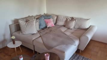 A living room with a beige sofa, a small round table with a vase, and a patterned rug.