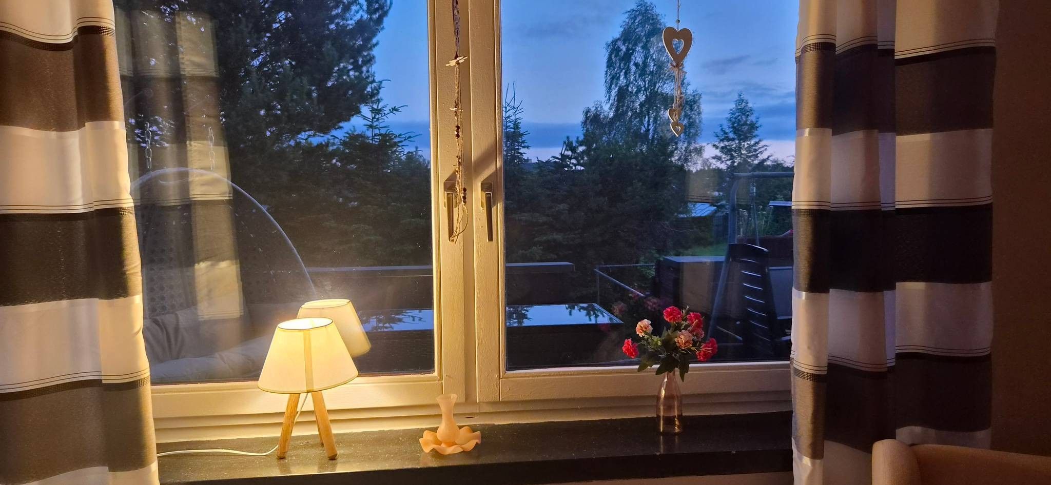 A room with a window, a lamp, and a vase with flowers on the windowsill.