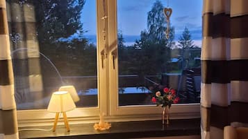 A room with a window, a lamp, and a vase with flowers on the windowsill.
