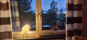 Ein Zimmer mit Fenster, einer Lampe und einer Blumenvase auf dem Fensterbrett.