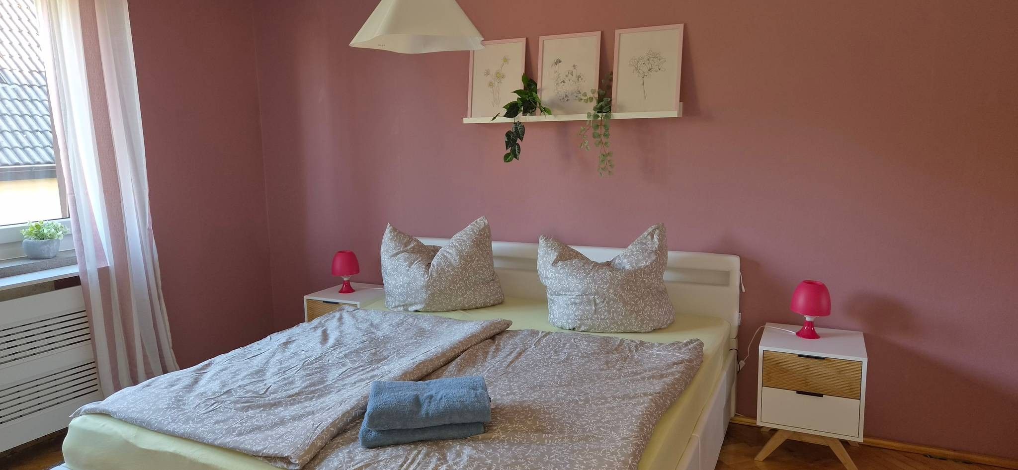 Ein Schlafzimmer mit einem Bett, Kissen, Nachttischen, einer Lampe und Wandbildern.