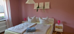 Een slaapkamer met een bed, kussens, nachtkastjes, een lamp en decoratie aan de muur.