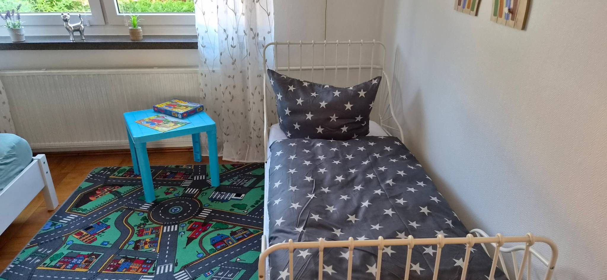 Habitación infantil con una cama, una mesita azul y un tapete de juegos colorido.