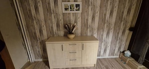A wooden cabinet with three drawers, a vase with dried plants on top, and a framed picture on the wall.