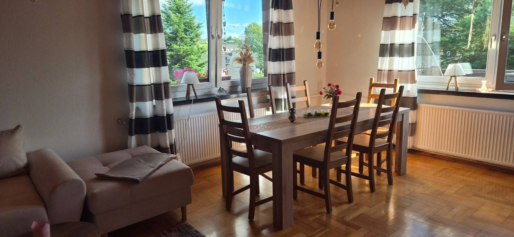 Ein Essbereich mit Tisch und Stühlen, einer Couch und einem Fenster mit Vorhängen.