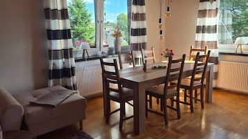 Ein Essbereich mit Tisch und Stühlen, einer Couch und einem Fenster mit Vorhängen.