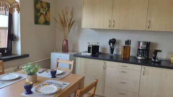 Cocina compacta con armarios de madera, una mesa de comedor para dos personas y una cafetera sobre la encimera.