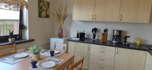 A compact kitchen with wooden cabinets, a dining table set for two, and a coffee maker on the counter.