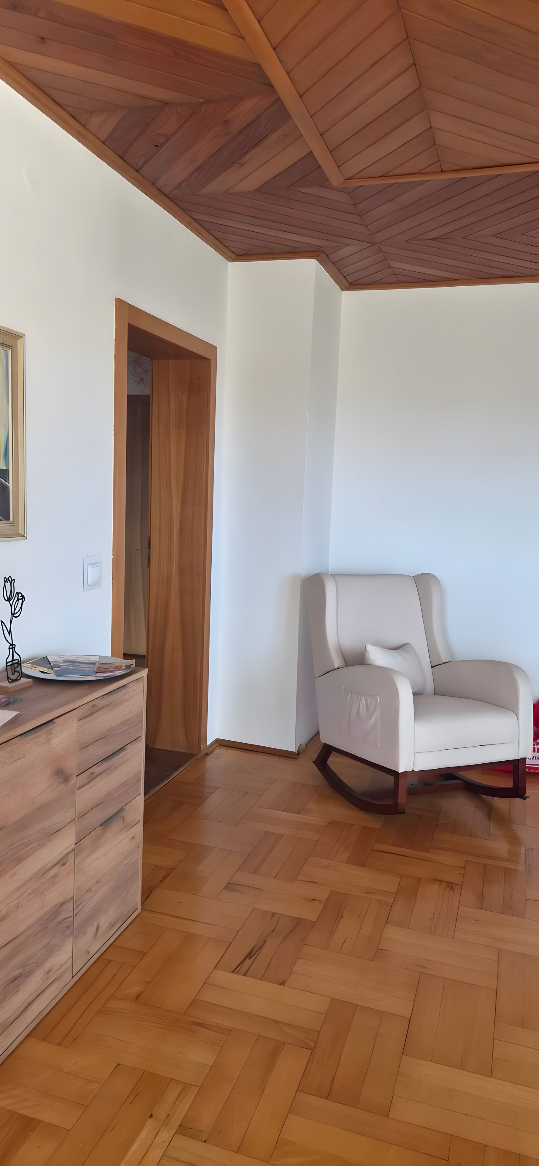 A room with a wooden herringbone floor, a white sofa, and a wooden cabinet.