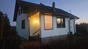 A single-story house with a sloped roof, a chimney, and a lit exterior light.