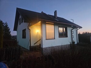 A single-story house with a sloped roof, a chimney, and a lit exterior light.