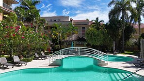 A pool area with lounge chairs, a bridge, and a building with a red-tiled roof. - Stay in our bright, spacious, and centrally located apartment at Ocean One (Cabarete)