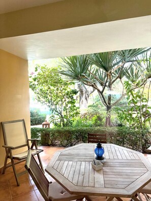 A wooden table with chairs, a blue lantern, and a view of a lush garden with trees and shrubs. - Stay in our bright, spacious, and centrally located apartment at Ocean One (Cabarete)