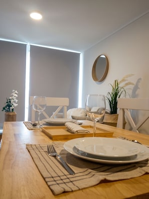 Un comedor con una mesa de madera dispuesta para dos personas, incluyendo platos, cubiertos y vasos.