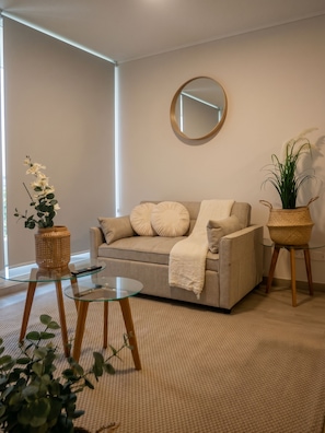 A modern living room with a sofa, a round mirror, and two side tables with plants. - Edificio Arturo Prat by Domus Travels (Santiago)