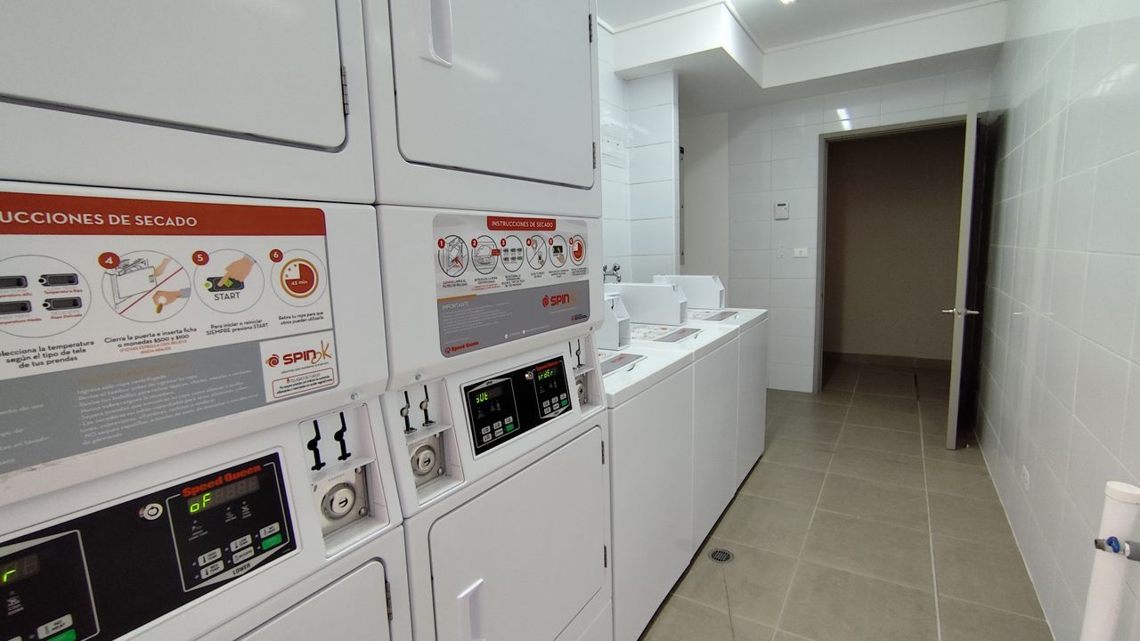 Un cuarto de lavandería con varias lavadoras, paneles de control y piso de baldosas.