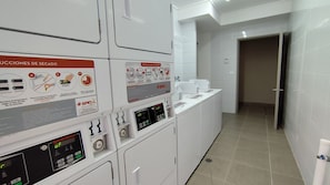 Un cuarto de lavandería con varias lavadoras, paneles de control y piso de baldosas.
